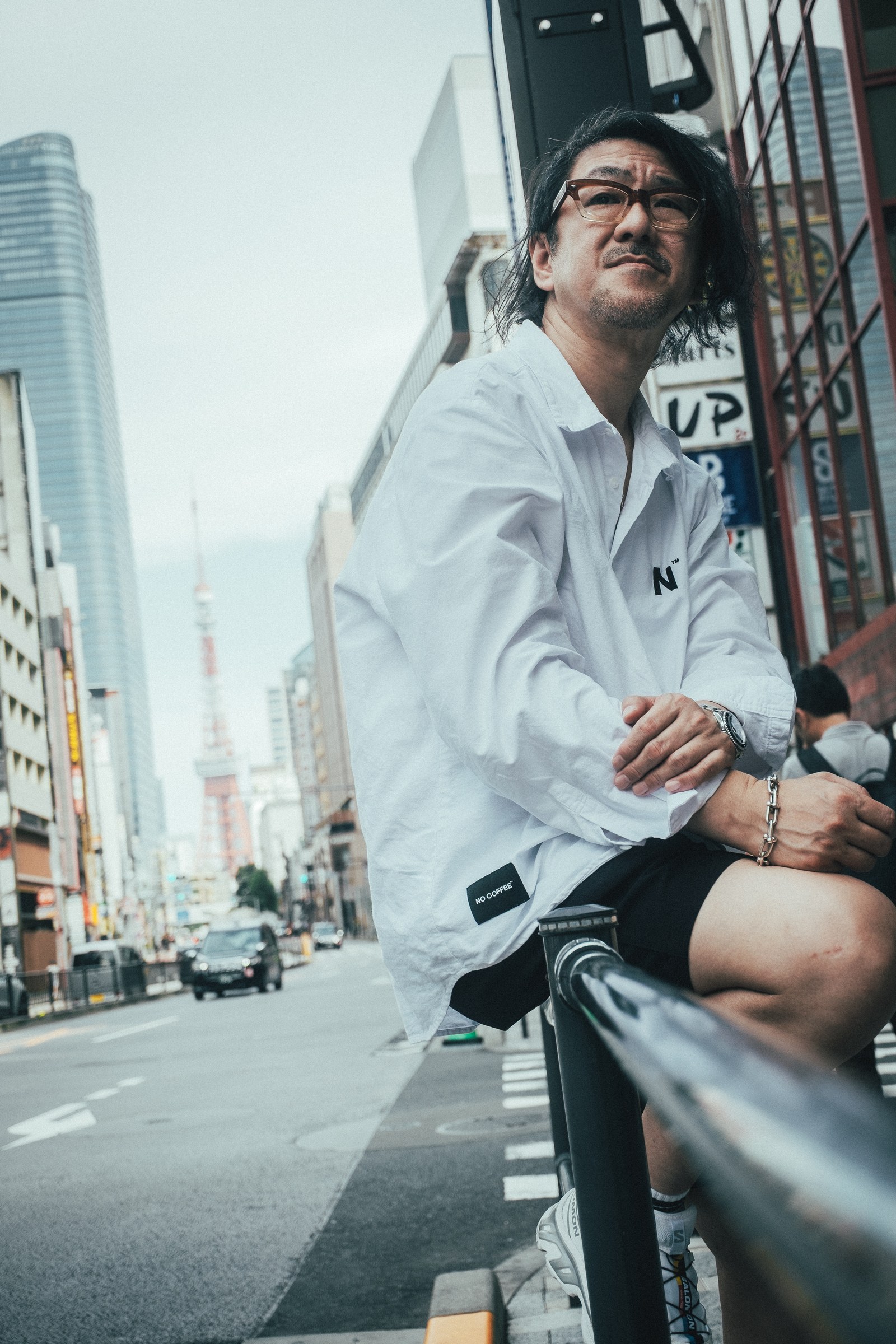 Tadahiro Koto in a white shirt, seated beside a city street